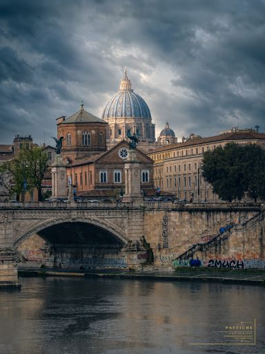 Historic buildings near a river, featuring a large dome under a cloudy sky.